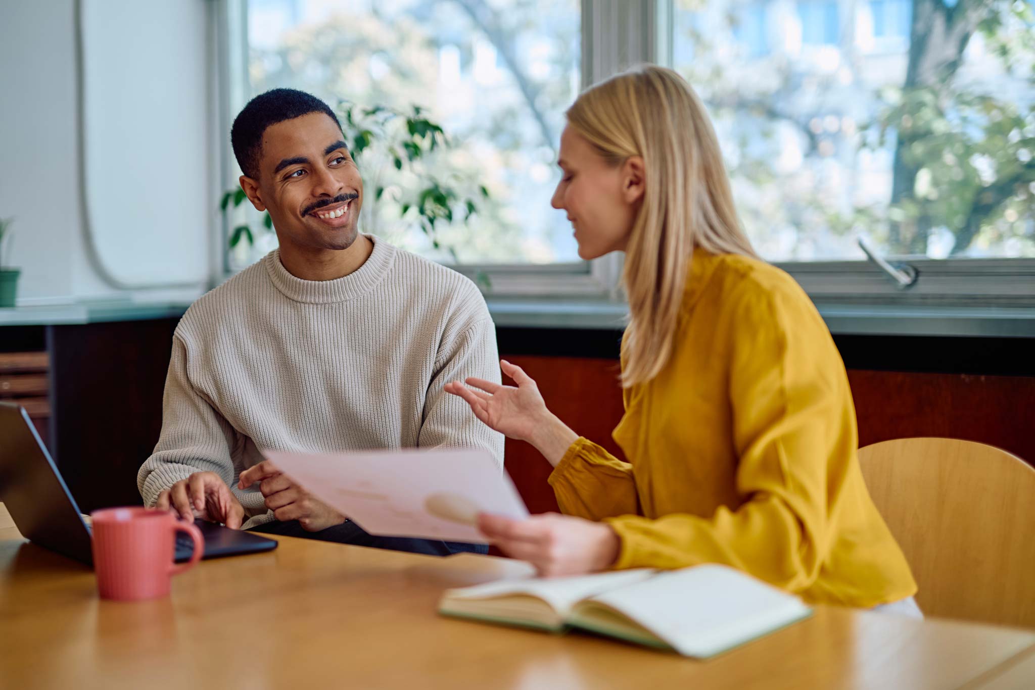 Two colleagues discussing documents together at a table in a bright office