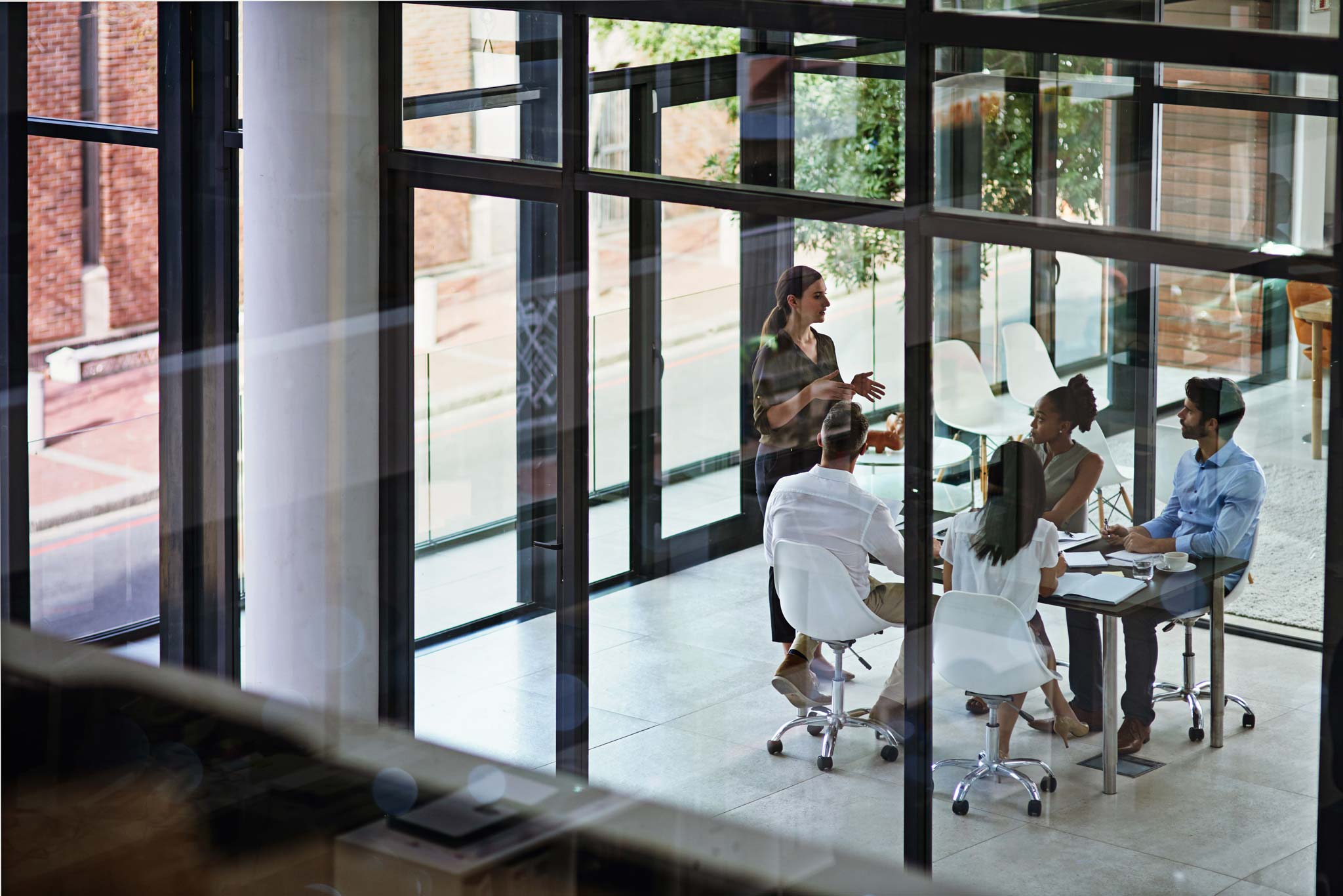 Colleagues gathered around a table for a meeting in a modern glass-walled office.